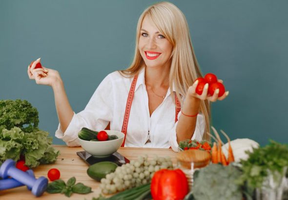 Healthy lifestyle concept with woman holding tomatoes and surrounded by fresh vegetables in a studio setting.